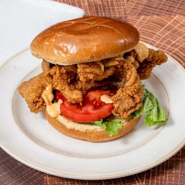 A Chick N' Friends fried chicken sandwich with lettuce, tomato, and sauce on a bun.