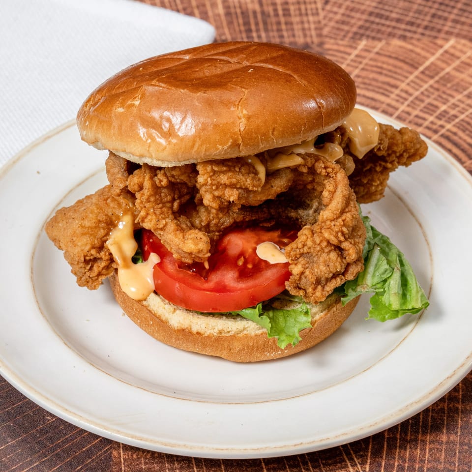 A Chick N' Friends fried chicken sandwich with lettuce, tomato, and sauce on a bun.
