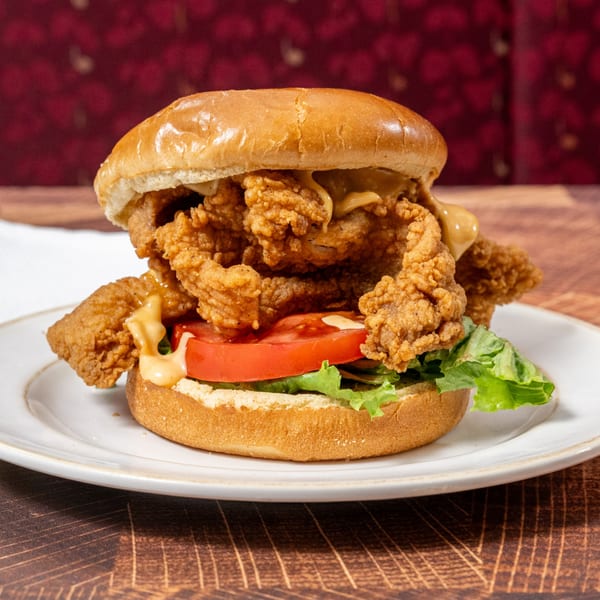 A Chick N' Friends fried chicken sandwich with lettuce, tomato, and sauce on a bun.