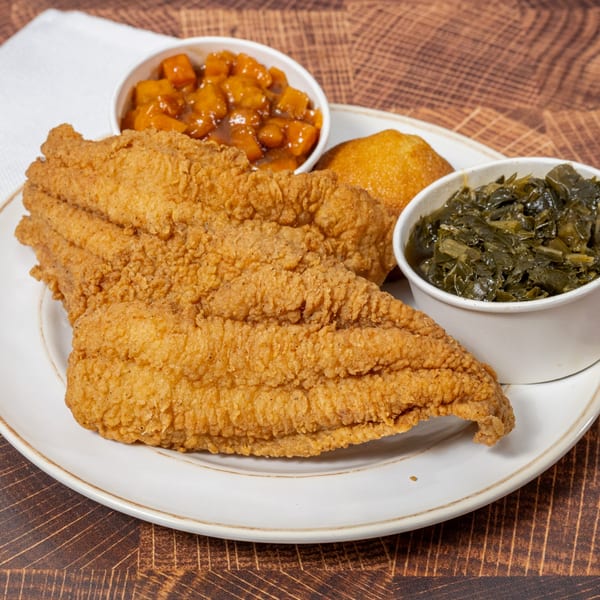 Fried fish fillets, candied yams, collard greens, and cornbread on a white plate from Chick N' Friends.