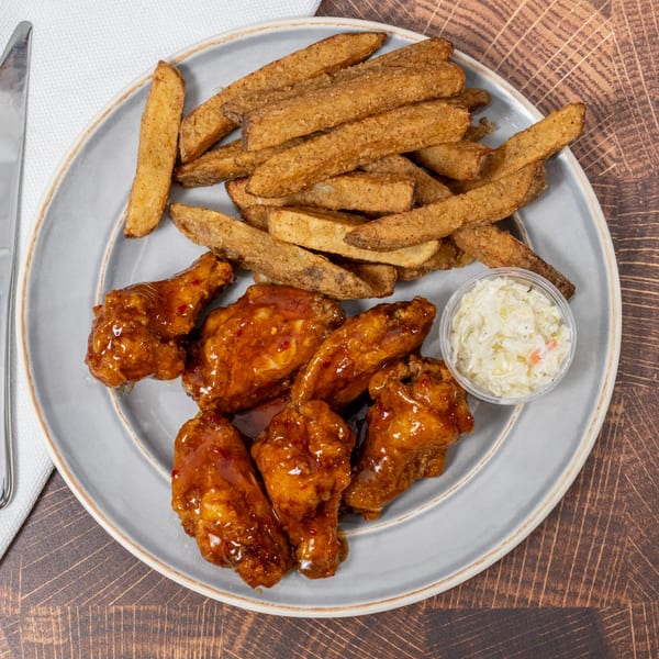 Chick N' Friends fried chicken wings with sauce, potato wedges, and coleslaw on a plate.