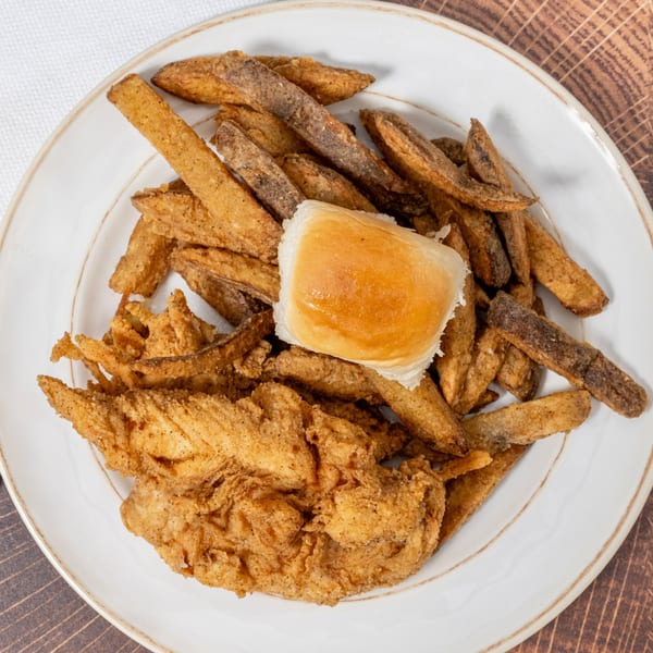 Chick N' Friends fried chicken tenders, seasoned fries, and a dinner roll on a white plate.