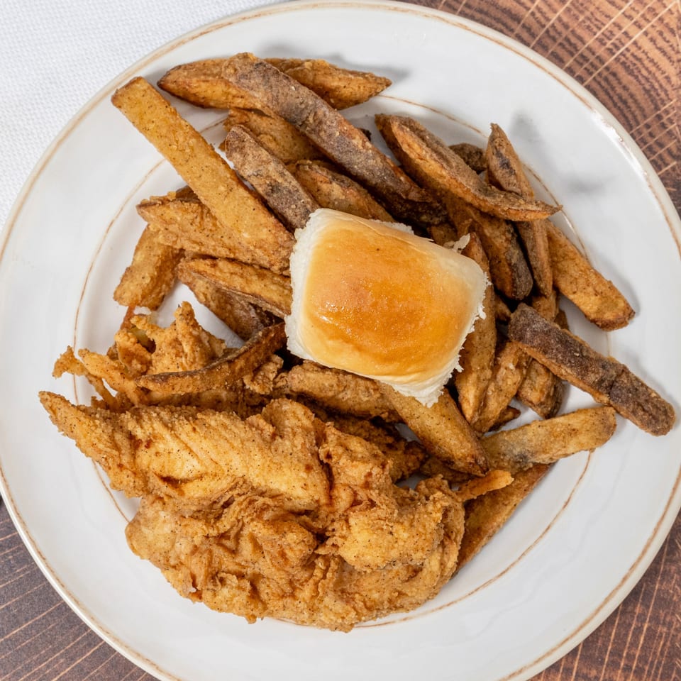 Chick N' Friends fried chicken tenders, seasoned fries, and a dinner roll on a white plate.