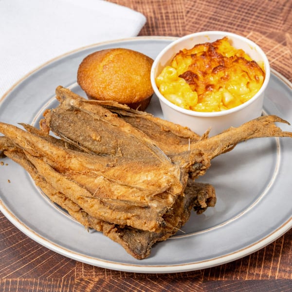 Fried fish fillets, a corn muffin, and baked mac and cheese on a gray plate.