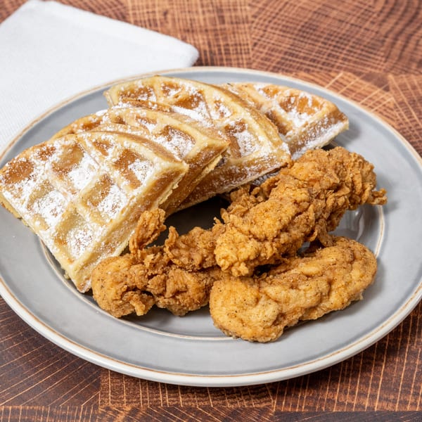 Chick N' Friends fried chicken tenders and powdered sugar waffles on a gray plate.