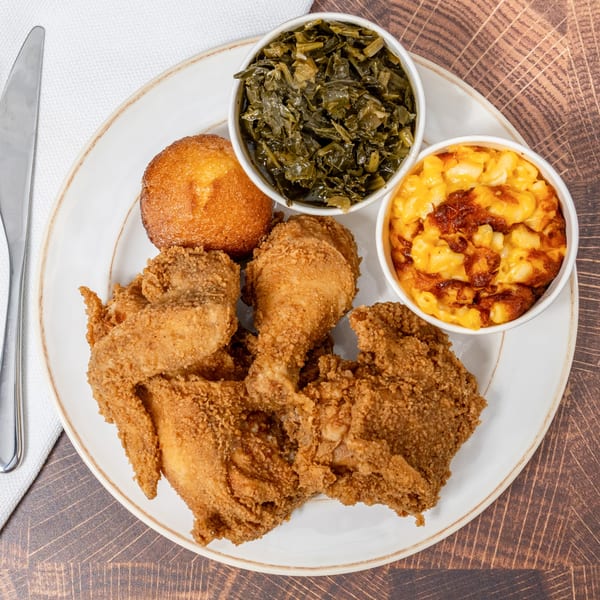 Fried chicken meal with collard greens, mac and cheese, and cornbread on a white plate.